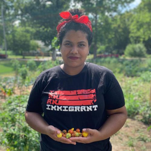 Vanessa holds colorful cherry tomatoes in her hands. She is wearing a shirt that says, 