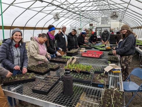 A dozen smiling people working with plants in a greenhouse.