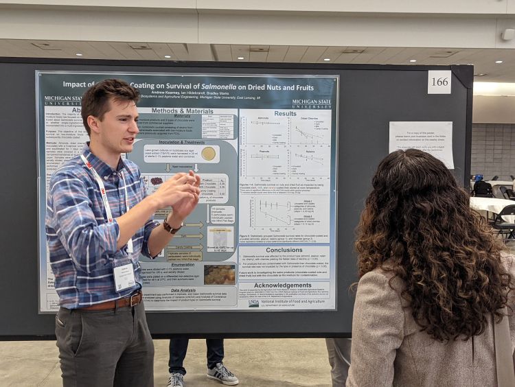 Andrew Kearney stands in front of his research poster while someone looks at it