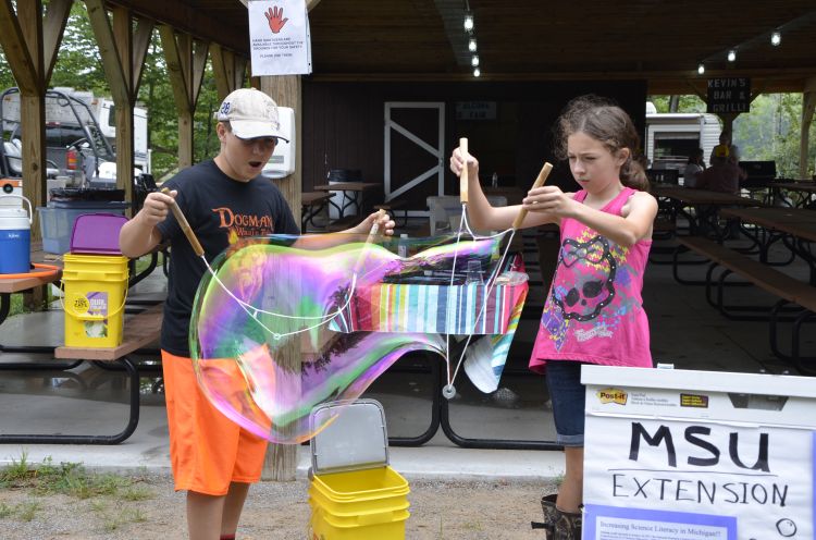 Two youth make a giant bubble together.