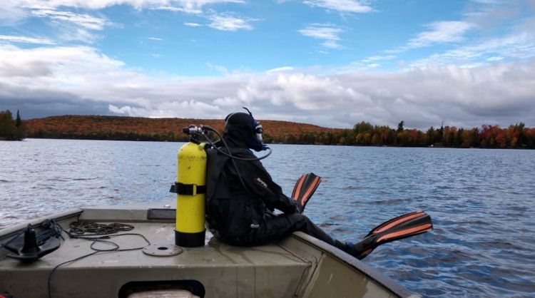A scuba diver dressed in diving gear sits on the side of a boat preparing to enter the water.