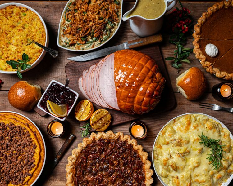 A top down photo of a dinner table with lots of cooked food on it including pie, potatoes, meat, and gravy.