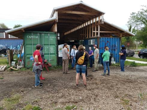 People standing in front of a barn. A washpack 'room' is made by building a roof over the space between 2 shipping containers.