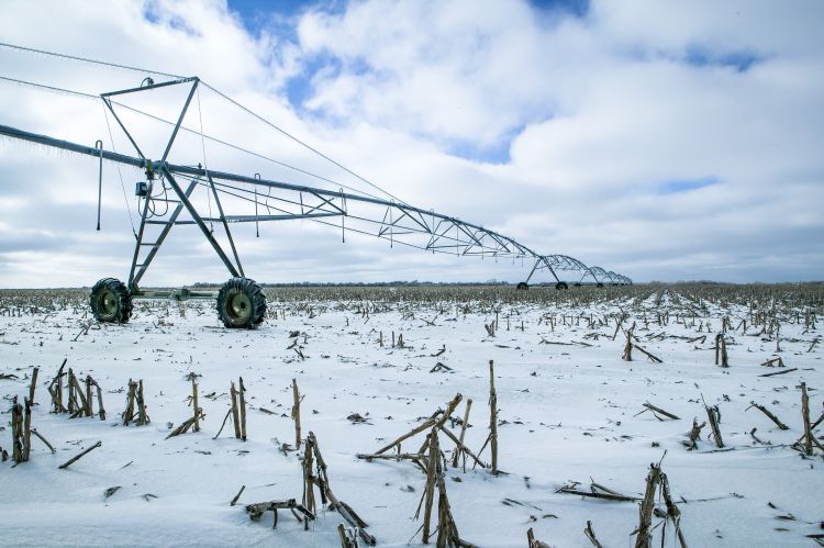 An irrigator sitting in a field during winter. The ground is covered with snow and harvested corn stalks.