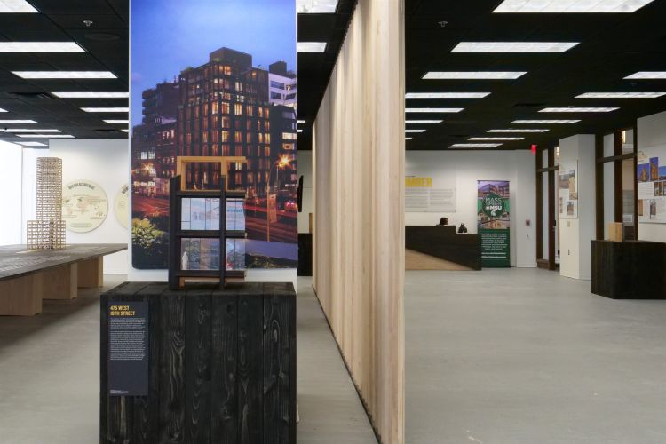 A small mockup of a mass timber building with a poster and photo of the building in real life behind it.