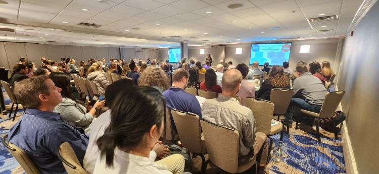 An audience of apiculture researchers and educators listen to a presentation in a conference room.