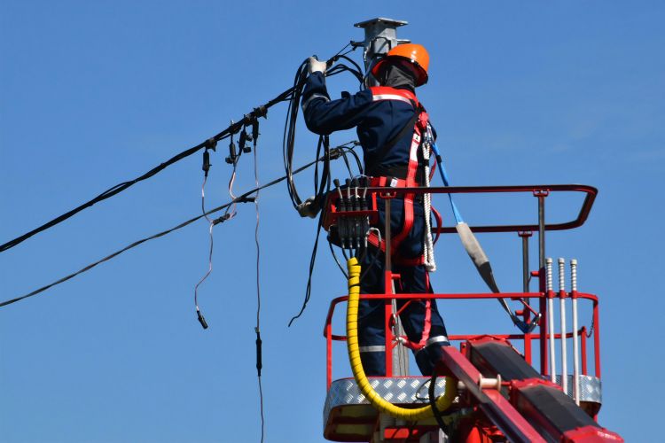 A man in safety gear up working on an electrical line.