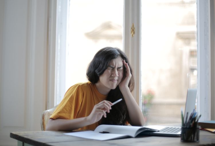 Woman sitting at a desk holding her head in pain.