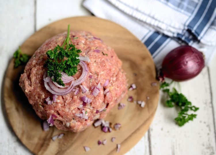 Raw ground turkey being prepared on a cutting board with onions and herbs.