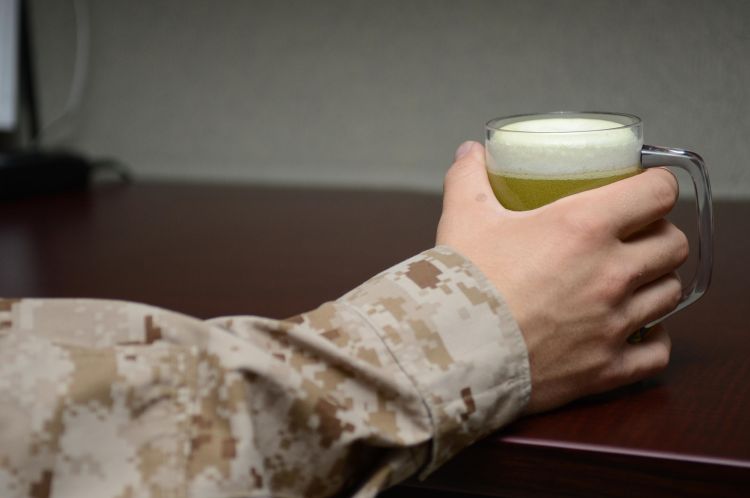 A soldier in their fatigues holding a beer.