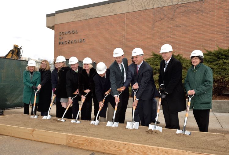 University and college leaders and donors wearing white hard hats hold shovels in dirt representing the official groundbreaking of the renovations to the MSU School of Packaging building.