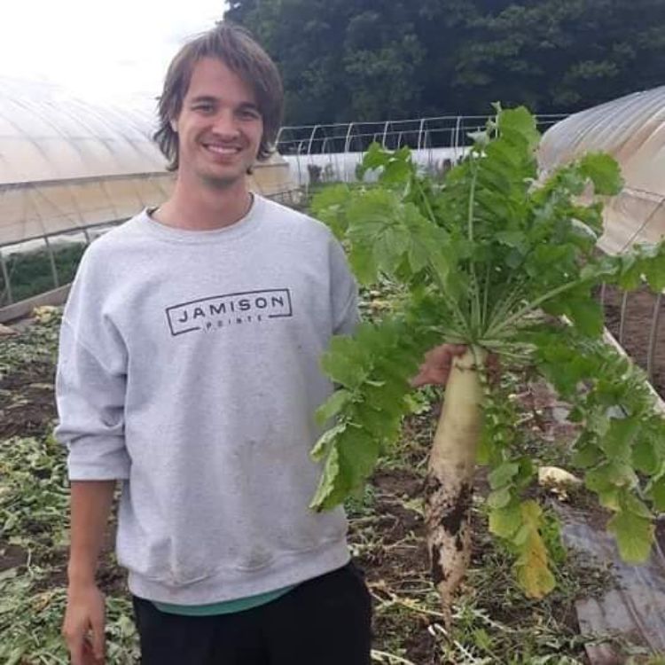 A young man holding a crop in a greenhouse