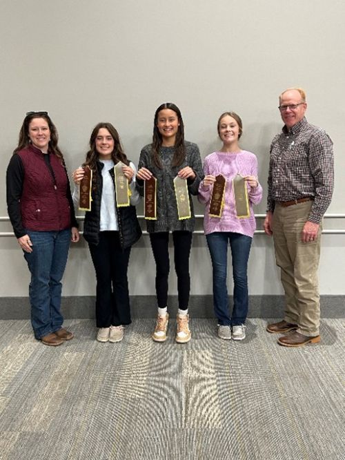 Three young women holding up ribbons with two smiling adults on either end.