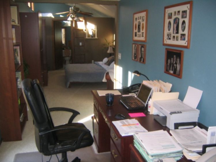 Desk with papers, computer and printer with bed in background