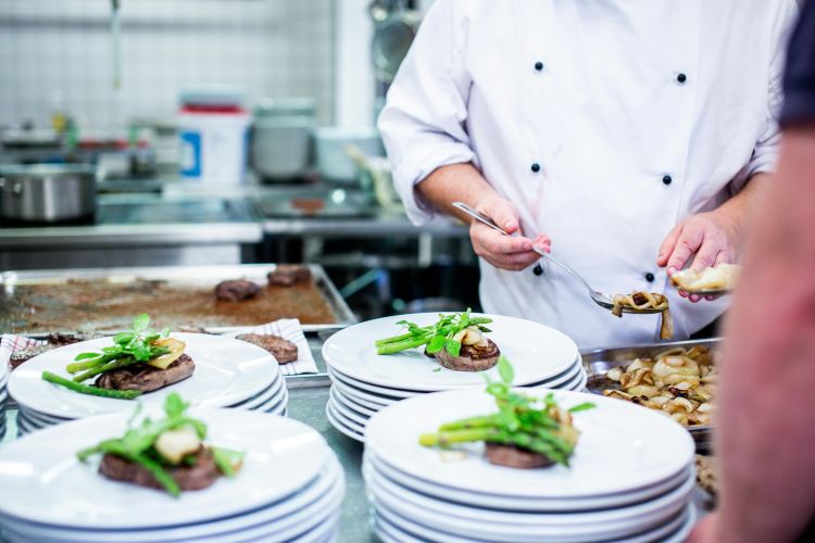 A photo of a chef preparing plates of food in a restaurant kitchen.