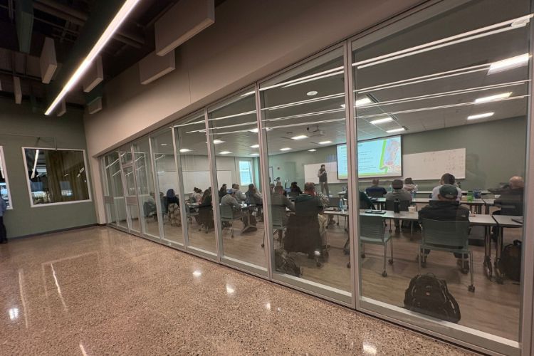 a glass wall in front looking into a classroom with people sitting at desks