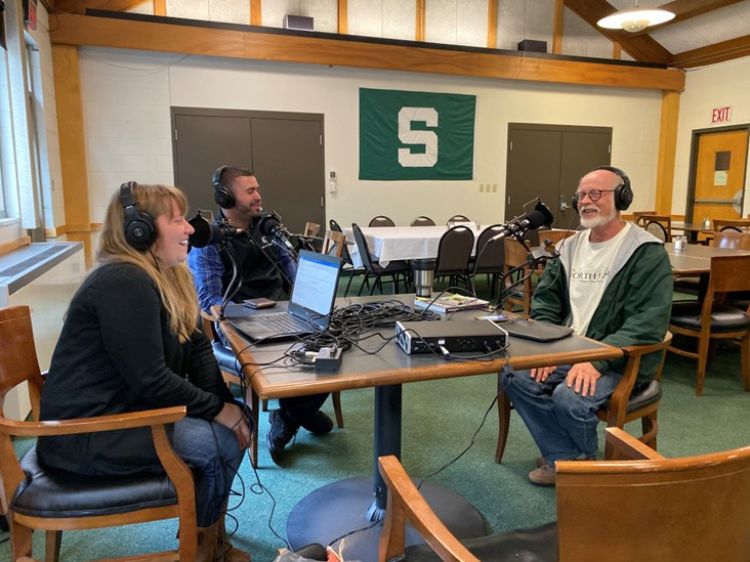 A group of people sitting around a table with podcast equipment.