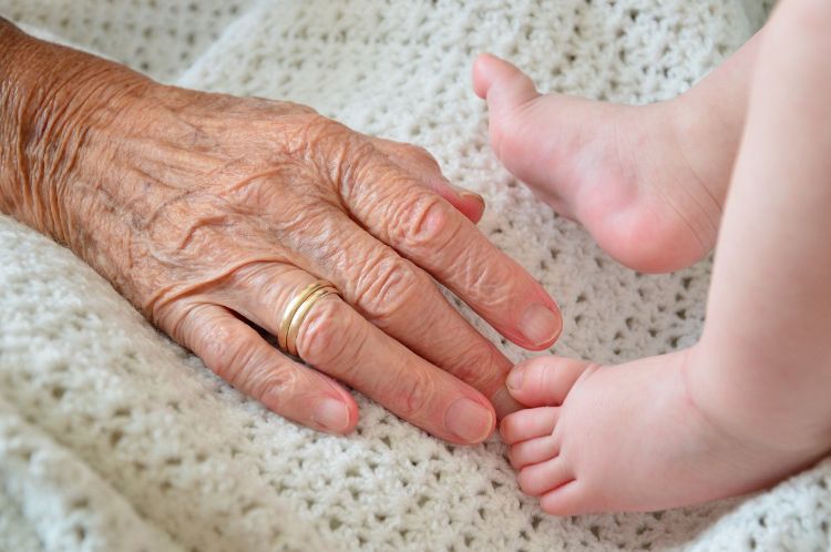 An elderly person holding an infant's foot.