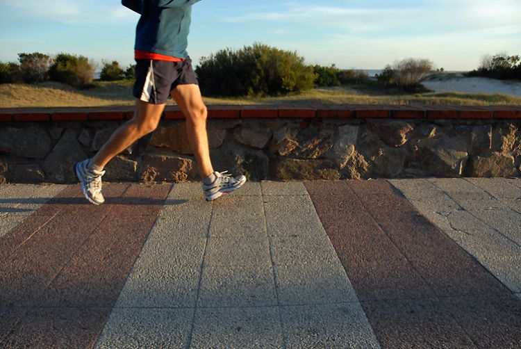 A bottom view of someone's legs running outside on a sidewalk.