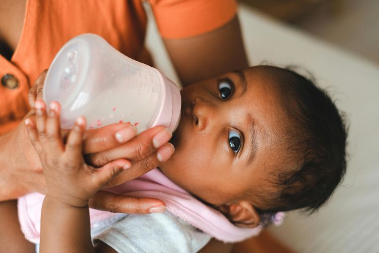 A photo of an infant being bottle fed while wearing a bib in a persons arms.