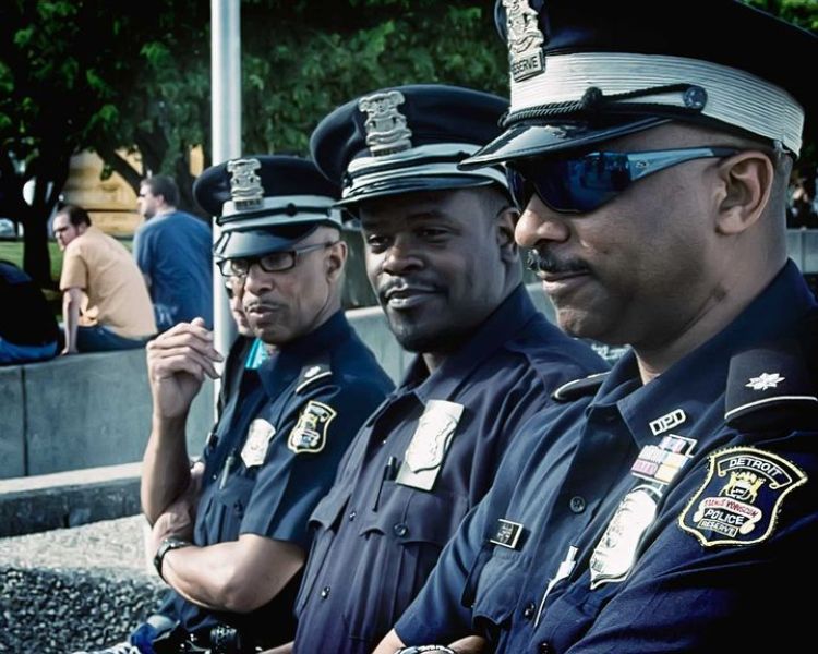 3 Detroit police officers in uniform sitting on a ledge outside