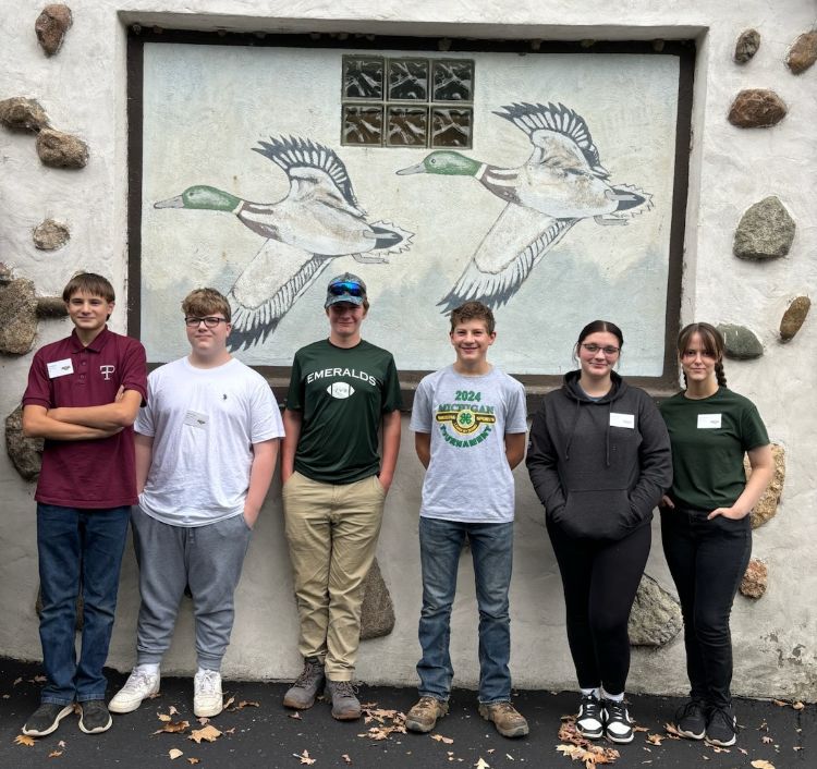 A mixed group of male and female teens standing against a backdrop with two ducks.