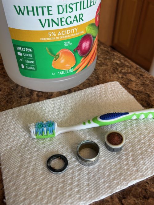 A photo of vinegar, a toothbrush and a disassembled aerator.