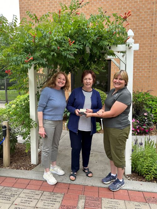 three women standing in front of a garden archway