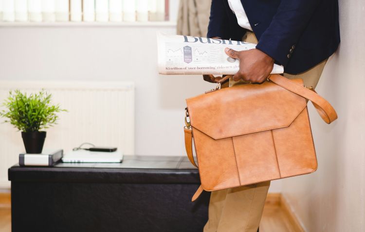 A portion of a man's body from the midsection down, showing a blue blazer, khakis and a briefcase.