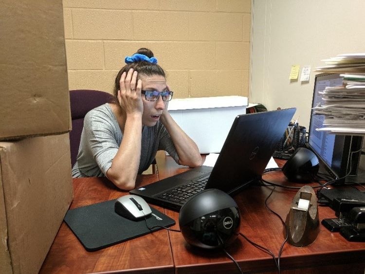 A woman sitting at a desk and looking at a computer, looking very stressed.