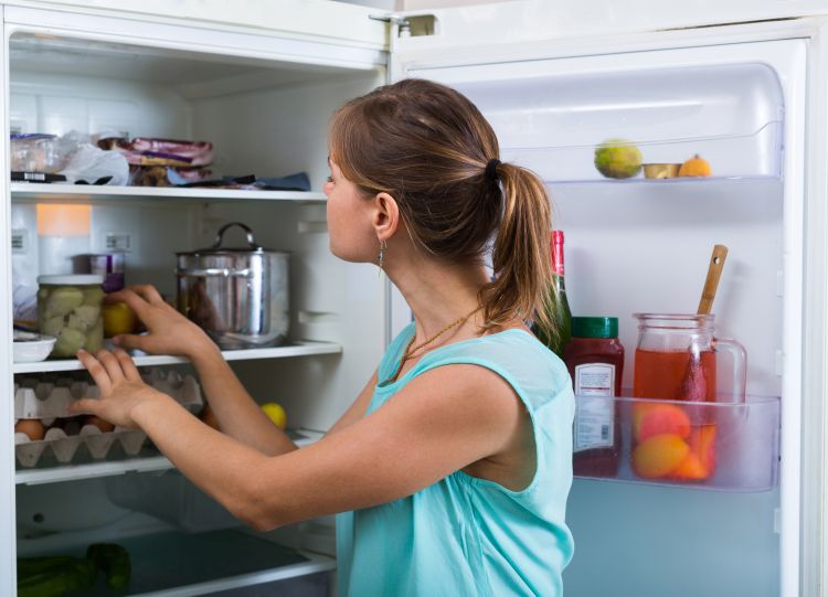 A woman looks at food in her refrigerator.