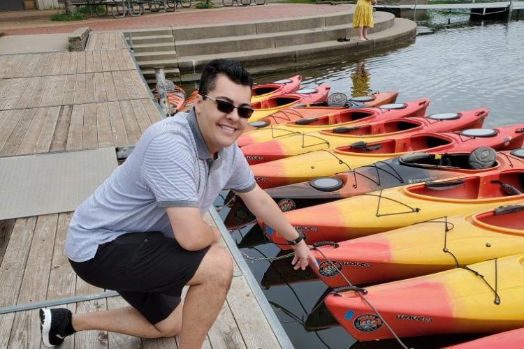 Cameron Webb poses by group of tied down orange and yellow kayaks