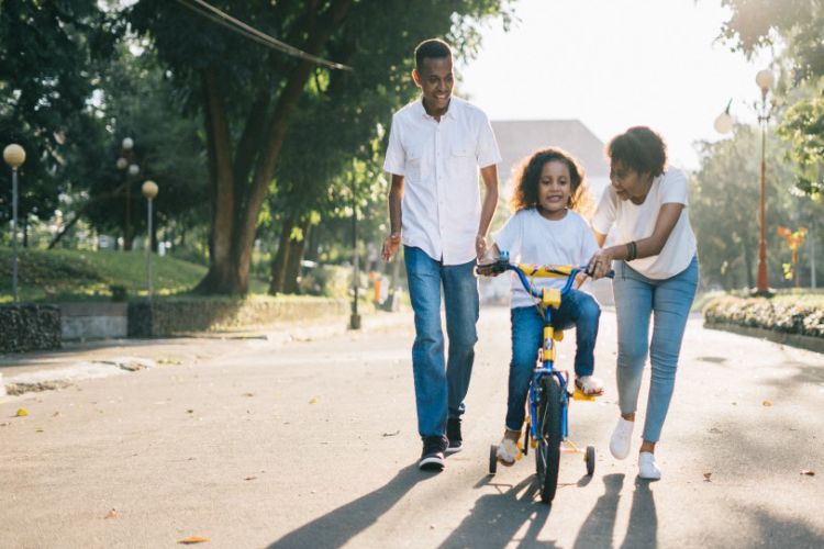 Mom and dad helping daughter ride bike.