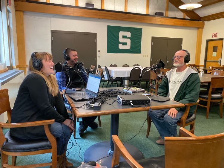 A group of people sitting around a table with podcast equipment.