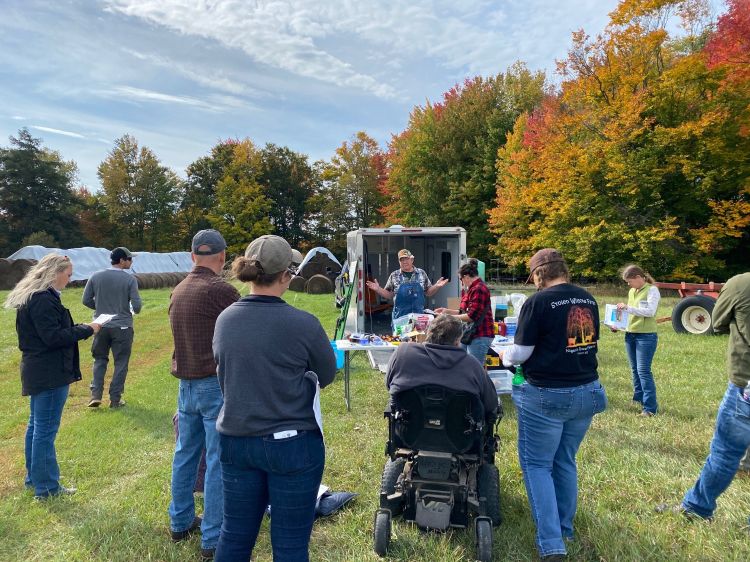 standing participants and one in a motorized wheelchiar observe a speaker in an outdoor setting