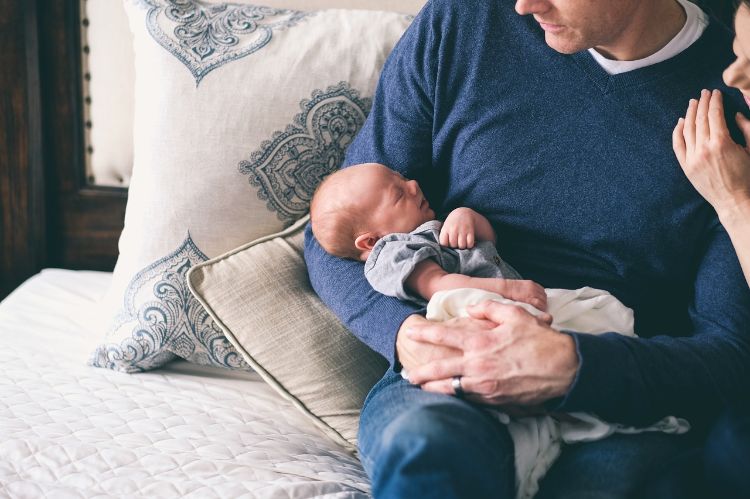 A man in a blue shirt holding an infant in his arms.