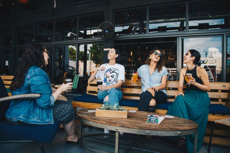 A group of four young adults sitting on a restaurant patio, socializing and drinking.