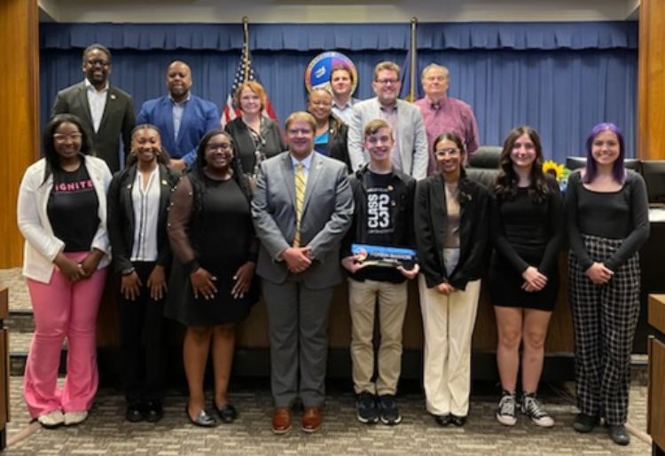 A diverse group of youth and adults standing in front of a desk.