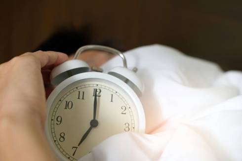 An alarm clock, sitting on a bed, in a pile of sheets