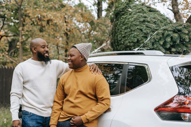 A father embracing a son near a car.