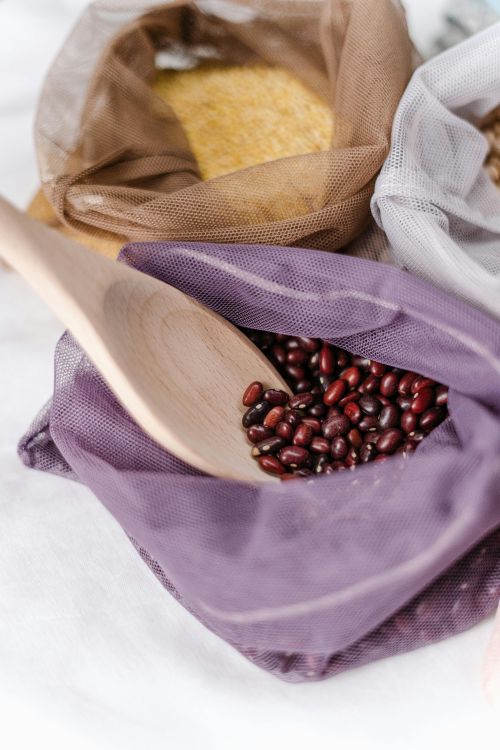 A photo of red beans with a wooden spoon in a purple mesh bag.