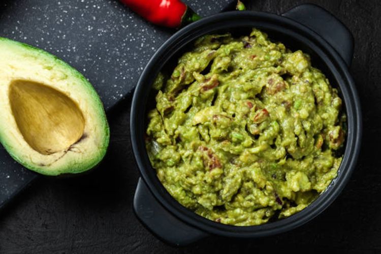 Half an avocado and a bowl of guacamole.