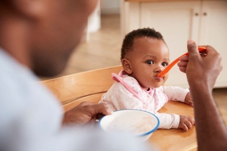 An adult feeding a small infant out of a bowl.