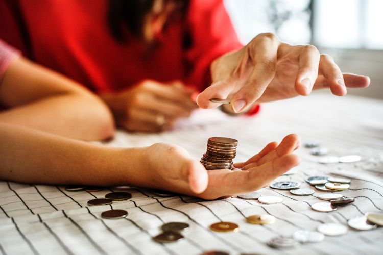 A hand with a stack of coins in it with another hand adding a coin to the stack.