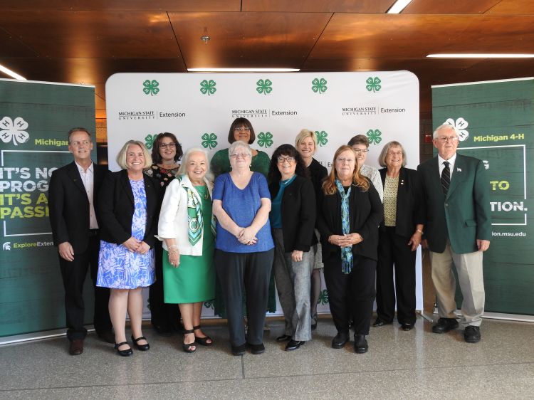 Twelve individuals standing in front of MSU Extension Michigan 4-H signage.