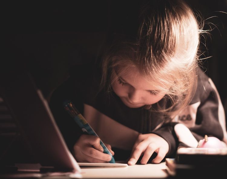 A small blonde girl writing with a pencil.