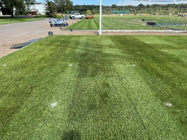 Finley mown turf in the foreground with a white post in the midground followed by more finely mown turf and a truck in the distance.