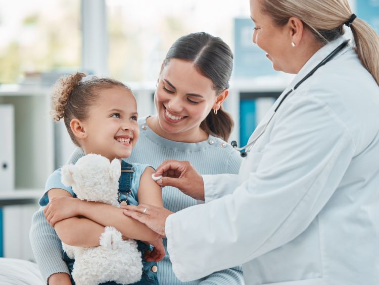 Photo of a doctor using a cotton ball on a young child's arm while administering an injection in a clinic.