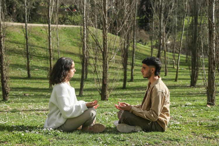 A man and woman sitting on the grass practicing mindfulness.