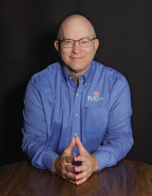 Kevin Dill smiling, wearing a blue button down shirt with the Purina logo on the chest.